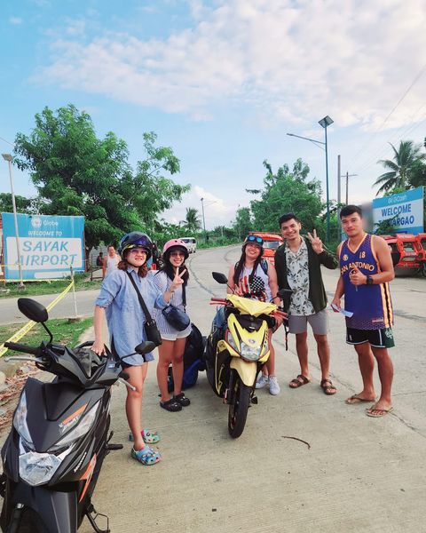 Travellers with rental scooters next to the Welcome to Sayak Airport sign
