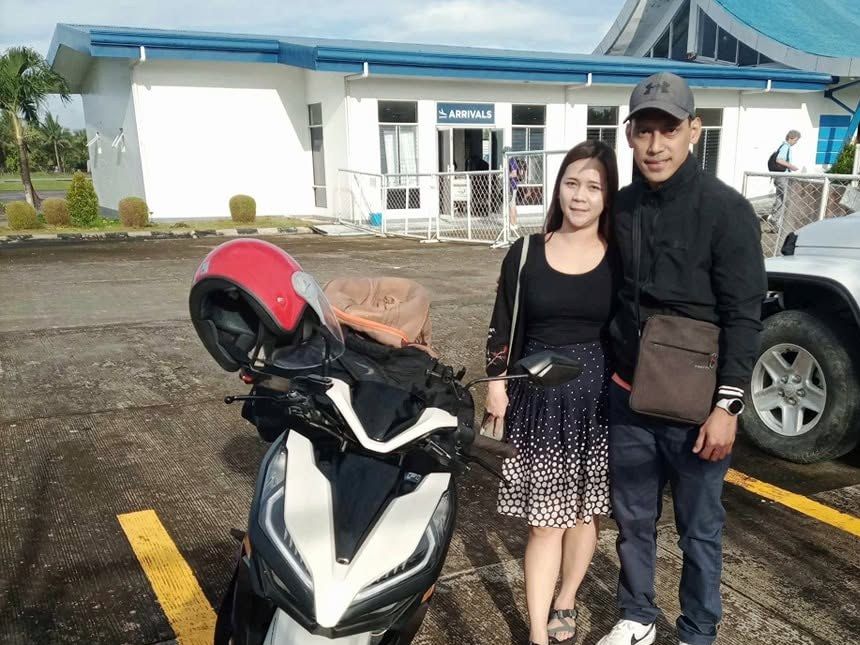 Couple beside a white Honda Click scooter outside the airport Arrivals building