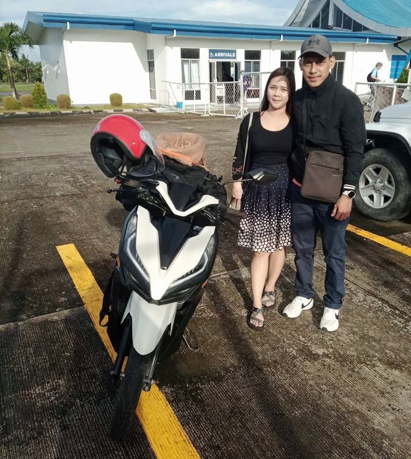 Couple beside a white Honda Click scooter outside the airport Arrivals building