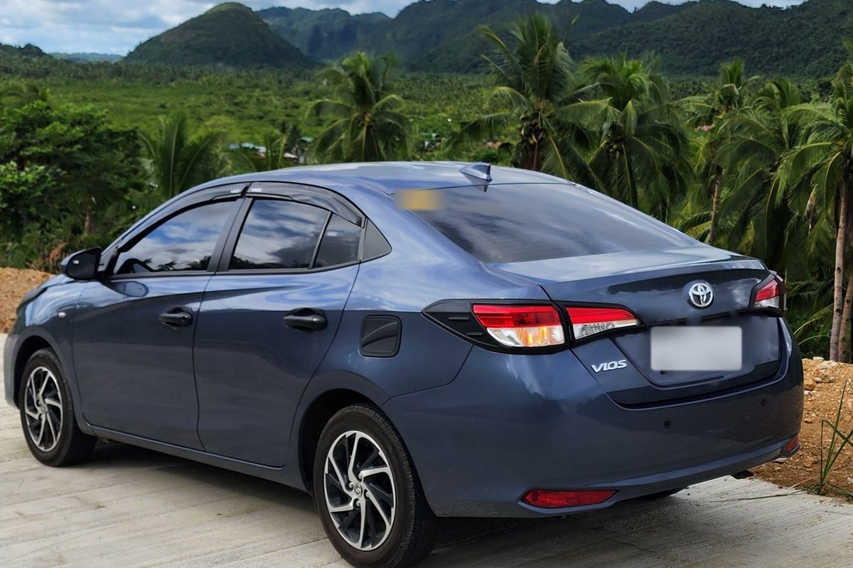 Blue-grey Toyota Vios parked on a hilltop overlooking jungle hills and coconut palms