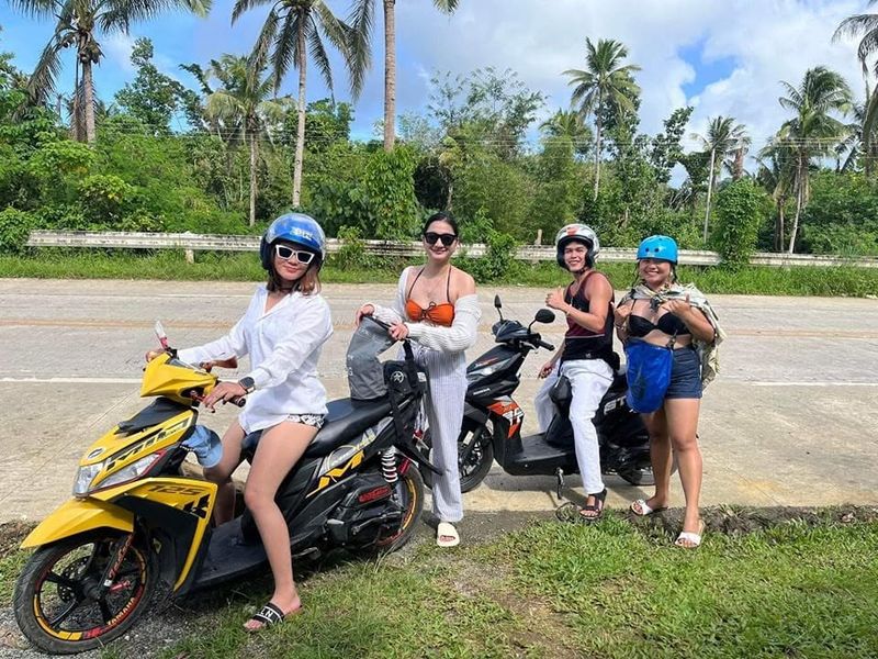 Four friends with rental scooters, including a yellow Yamaha Mio, on a sunny palm-lined road