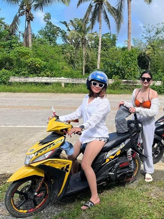 Four friends with rental scooters, including a yellow Yamaha Mio, on a sunny palm-lined road