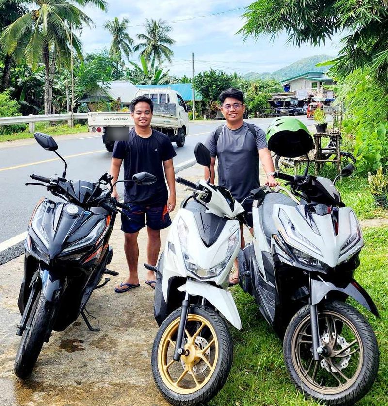 Two young men standing behind three Honda scooters by the roadside