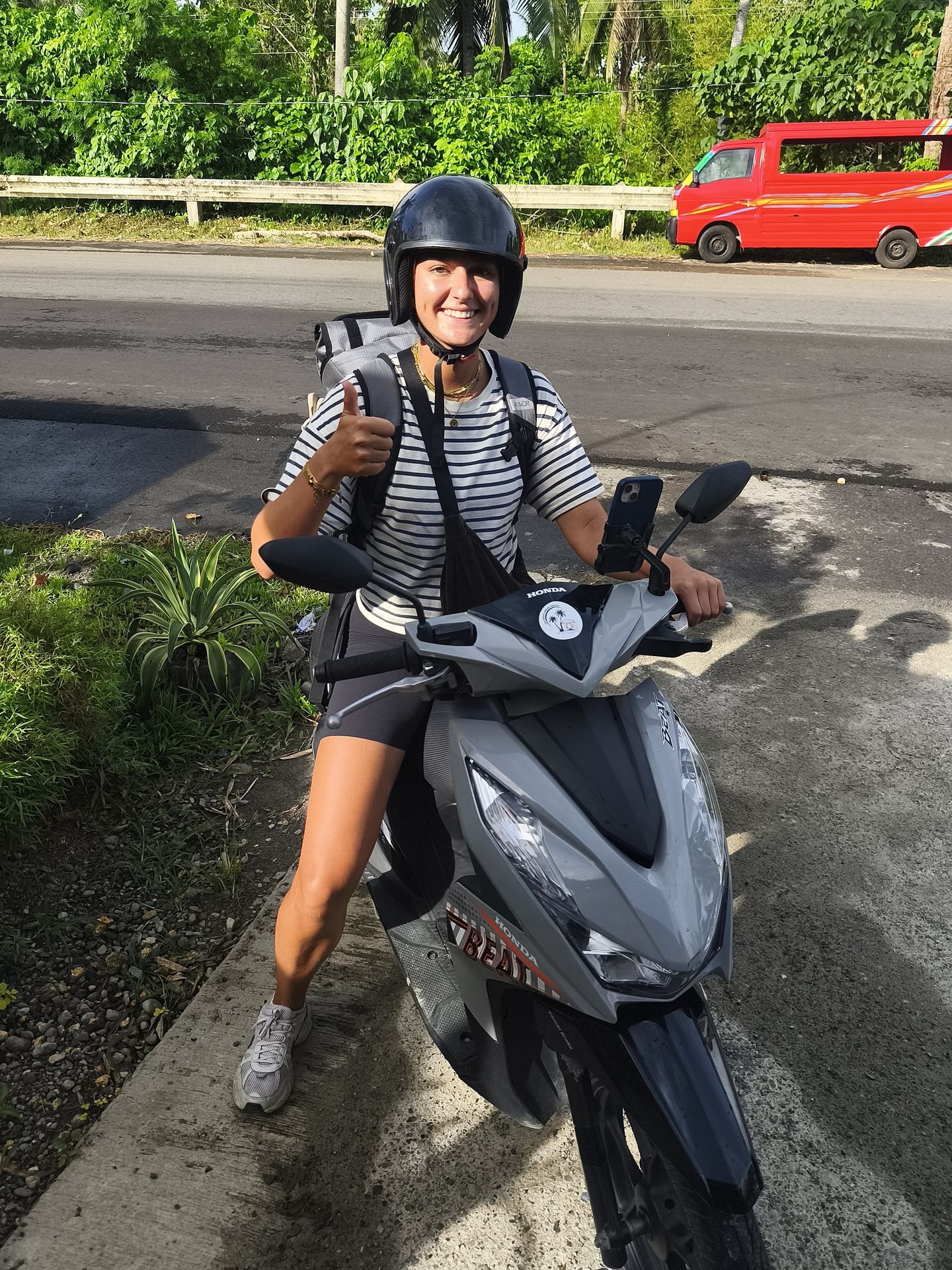 Smiling rider in a helmet giving a thumbs-up on a grey Honda BeAT