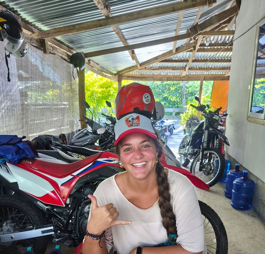 Smiling guest in a Siargao Rose cap giving a shaka at the shop desk, with dirt bikes behind