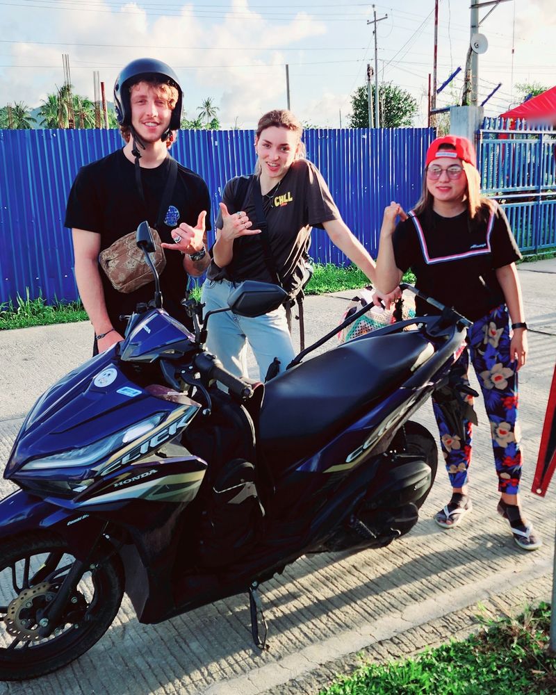 Three smiling people giving shakas beside a navy Honda Click scooter