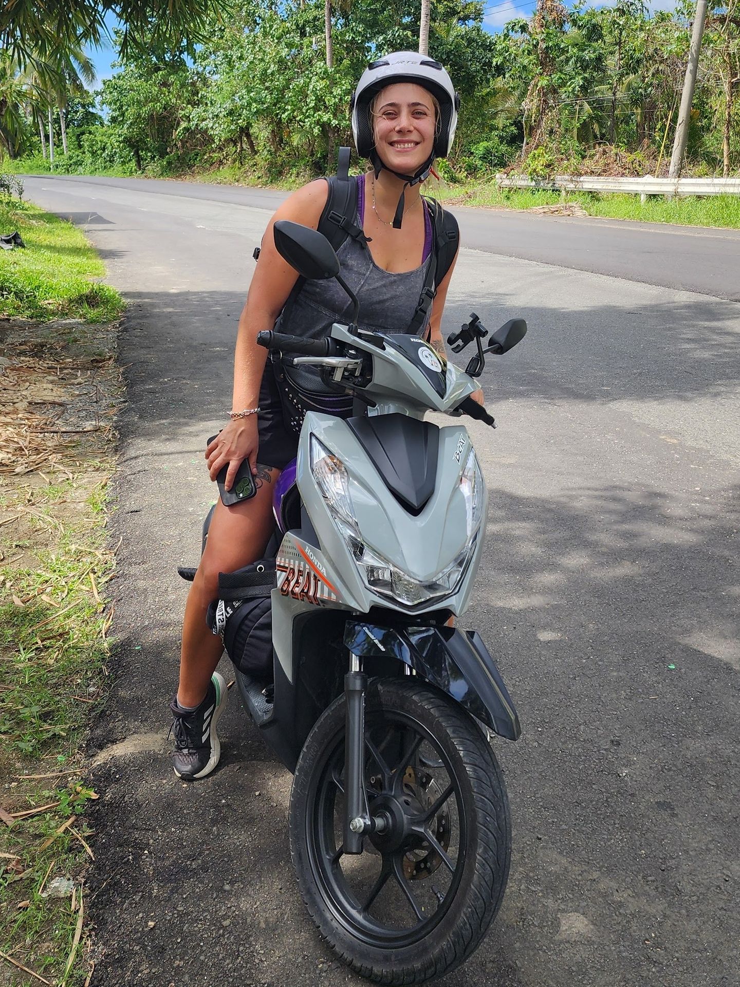 Smiling rider in a helmet on a grey Honda BeAT on a palm-lined road