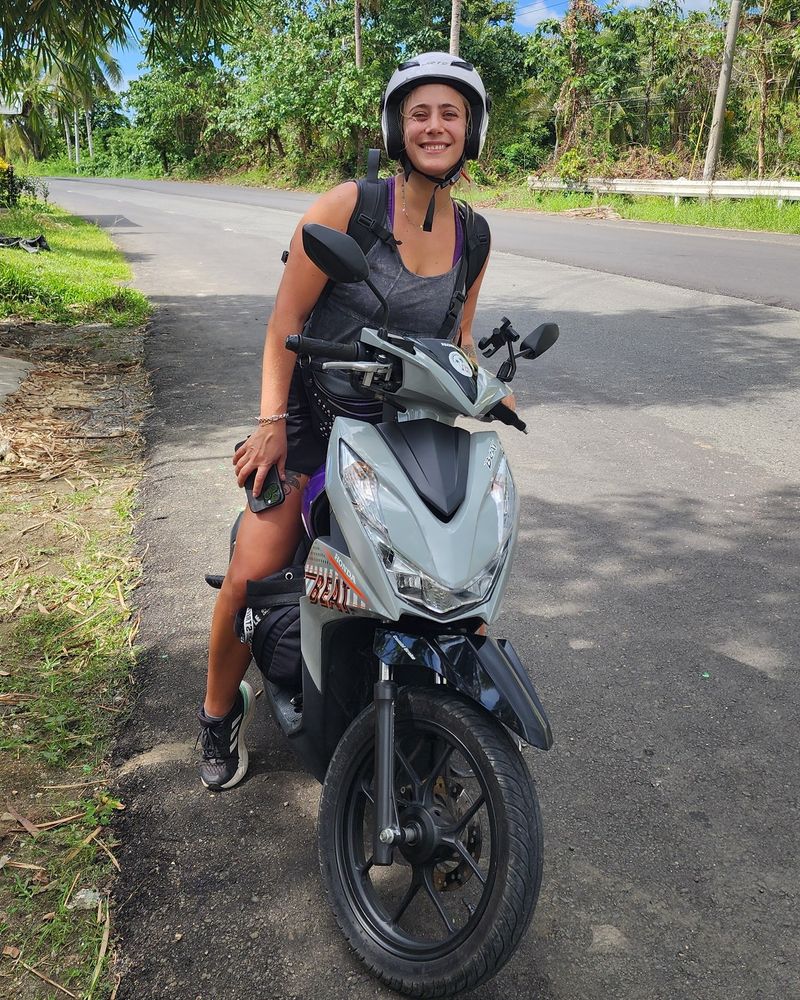 Smiling rider in a helmet on a grey Honda BeAT on a palm-lined road