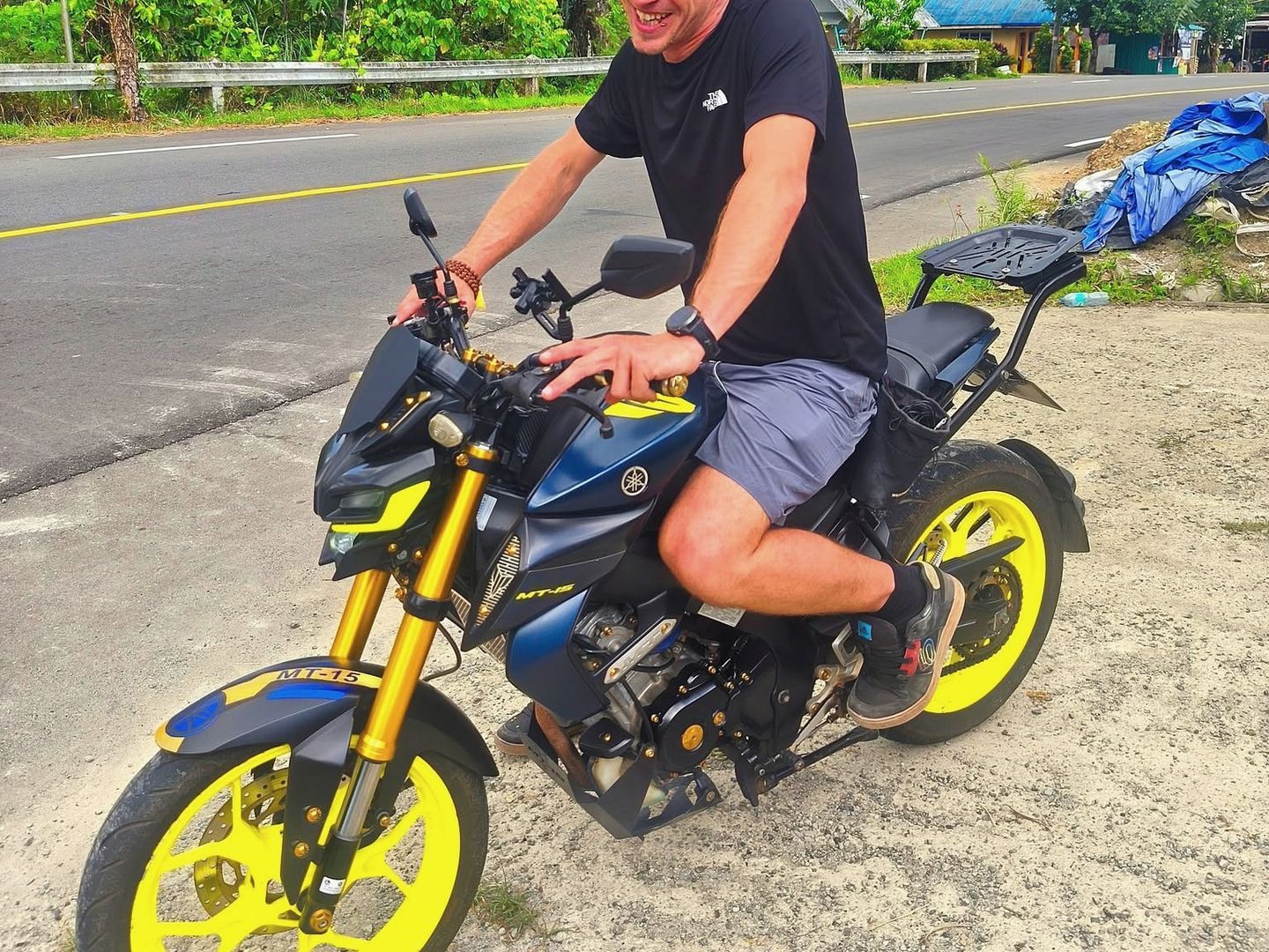 Laughing rider on a Yamaha MT-15 with yellow wheels beside a palm-lined road