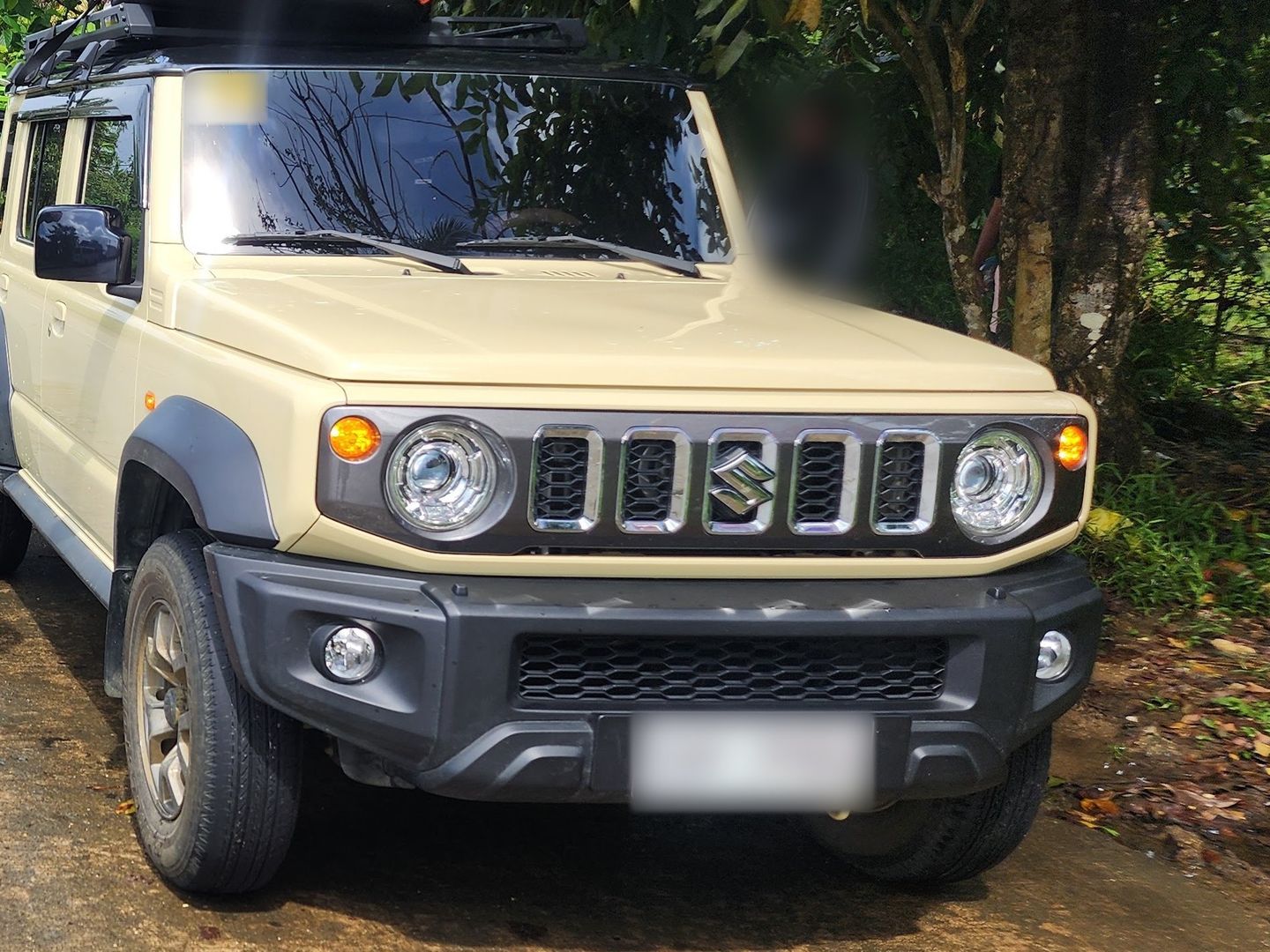 Beige five-door Suzuki Jimny parked beside tropical greenery