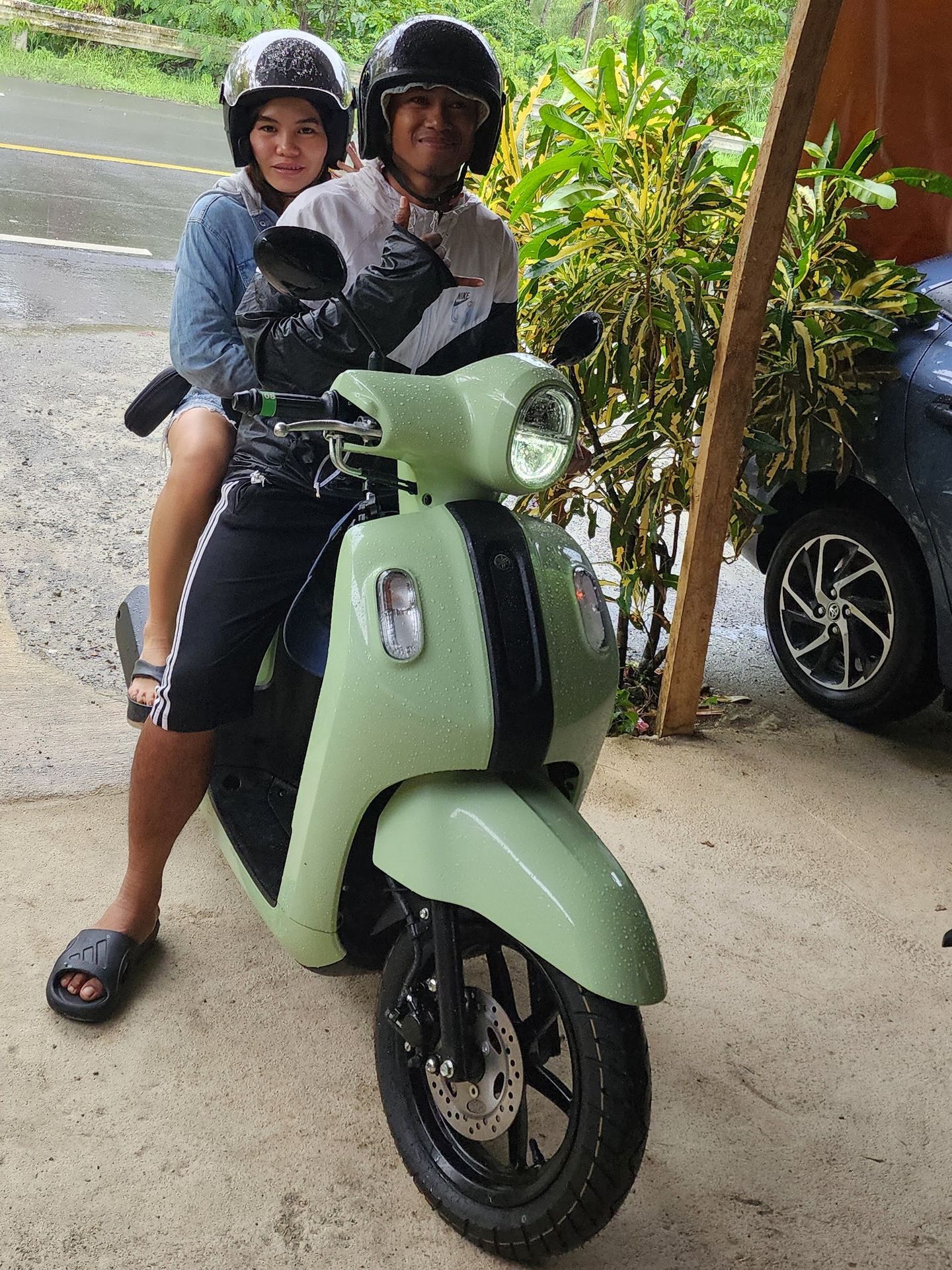 Mint-green Yamaha Fazzio scooter with two riders in helmets under the rental shed